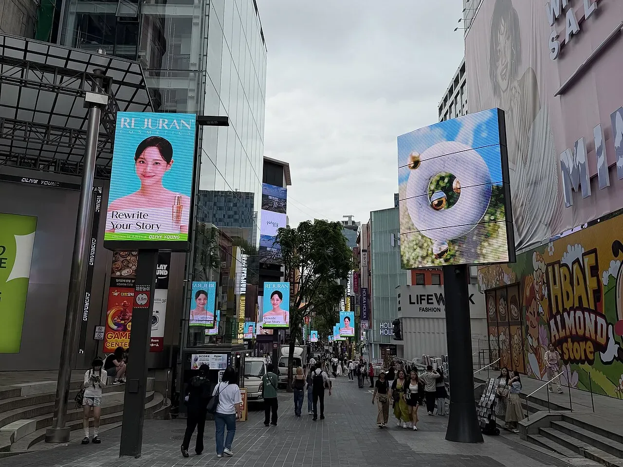 A wide pedestrian shopping street in Myeongdong lined with cosmetics shops and digital billboards