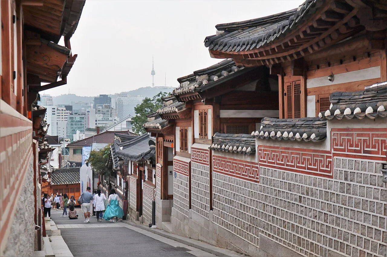 Traditional hanok rooftops and stone walls along a sloping lane in Bukchon Hanok Village, Seoul