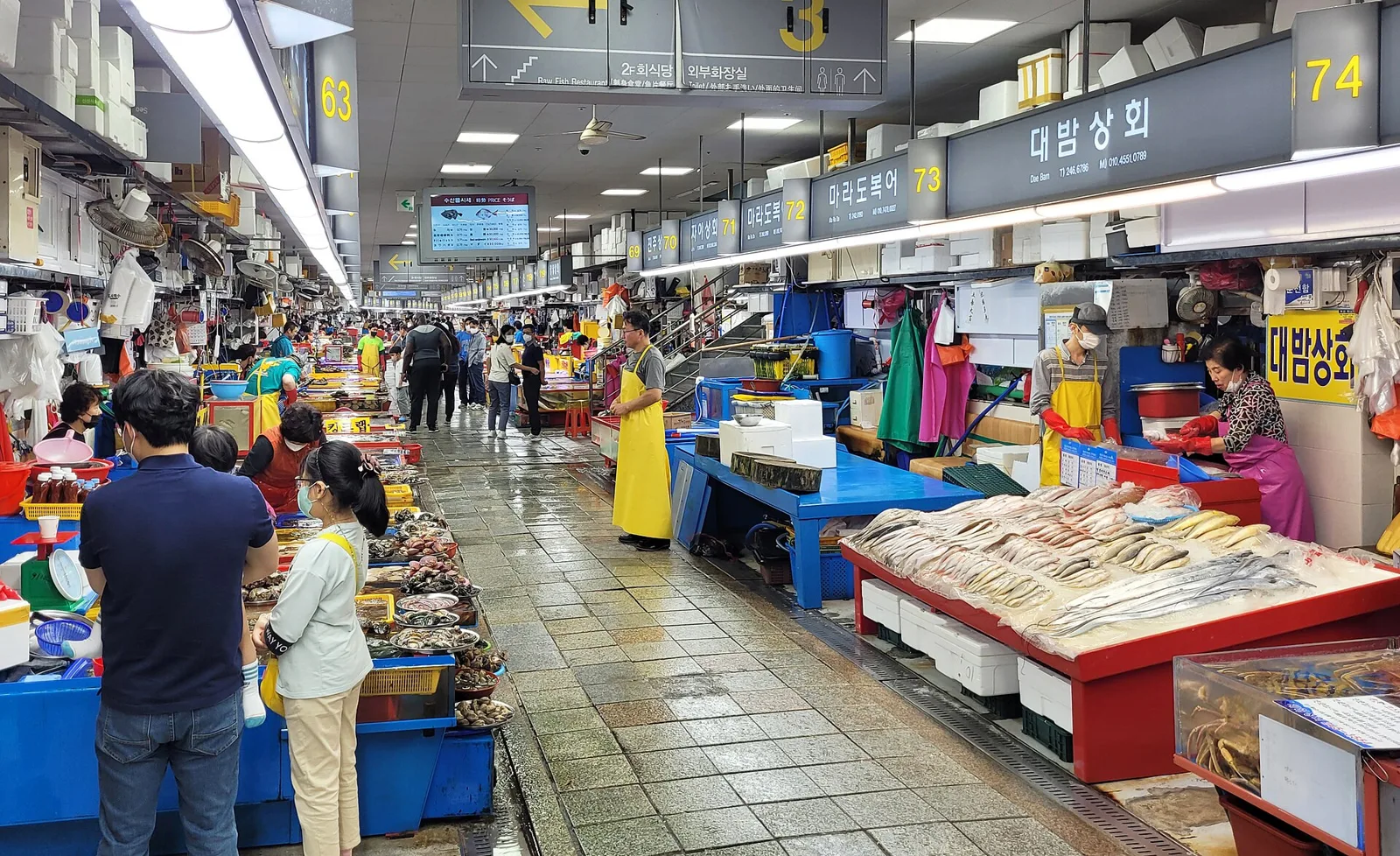 Shoppers walking through Jagalchi fish market in Busan, with stalls of dried and fresh fish under hanging signs