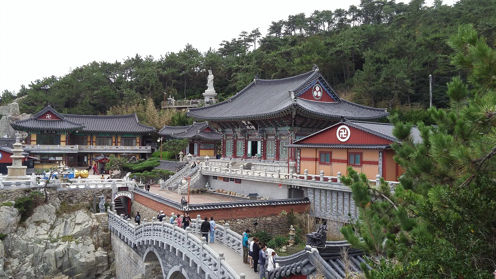 Haedong Yonggungsa temple buildings on rocks above the sea, with a stone bridge and pine trees
