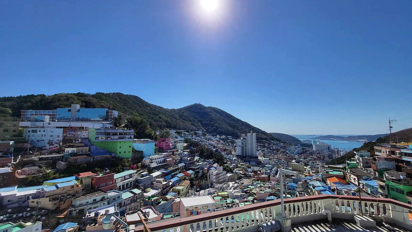 Wide view over the colorful rooftops of Gamcheon Culture Village from a viewing terrace, with mountains and sea in the distance
