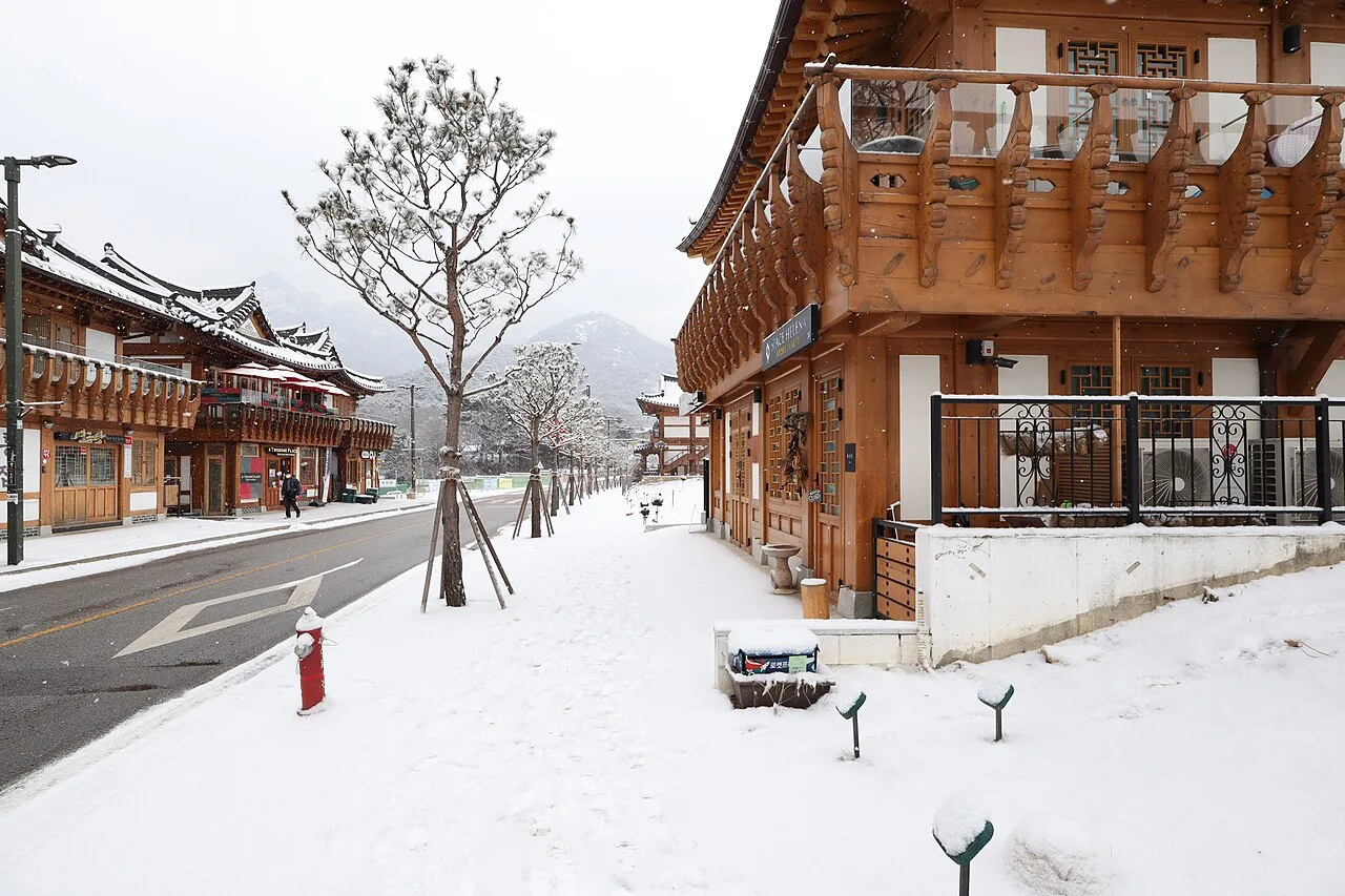Eunpyeong Hanok Village under snow, with two-storey wooden hanok along a wide street and mountains behind