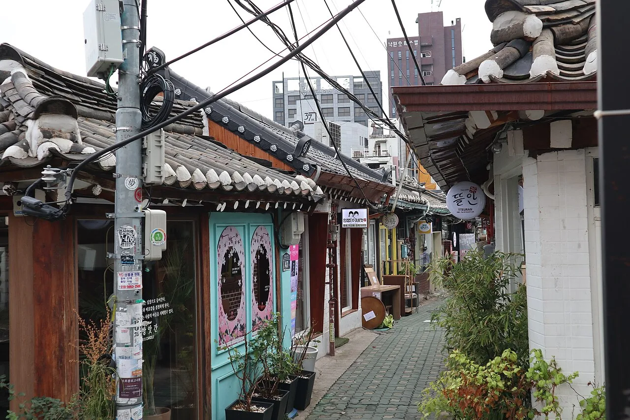 A lane in Ikseon-dong with hanok rooftops, small shops, overhead wires and a turquoise shopfront