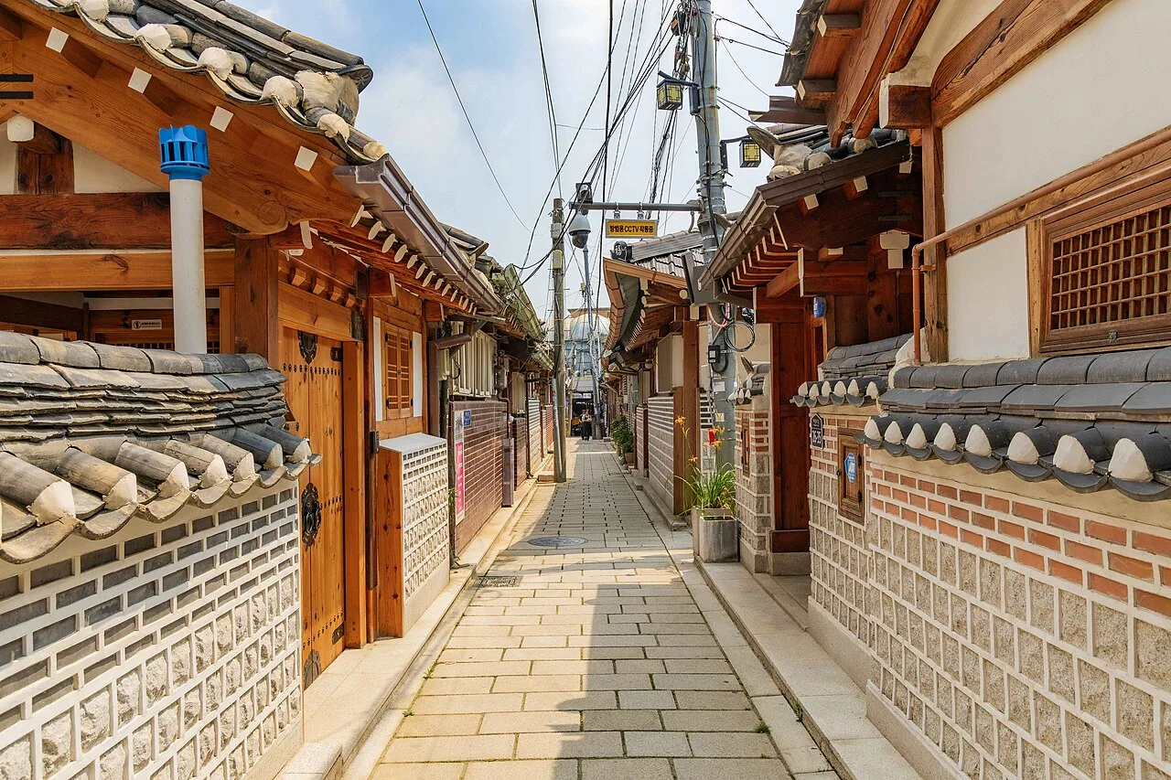 A narrow lane in Seochon's Nuha-dong with low hanok roofs, potted plants and small houses on both sides