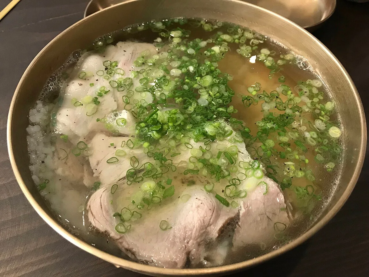 A bowl of clear pork gomtang soup topped with sliced pork and green onions