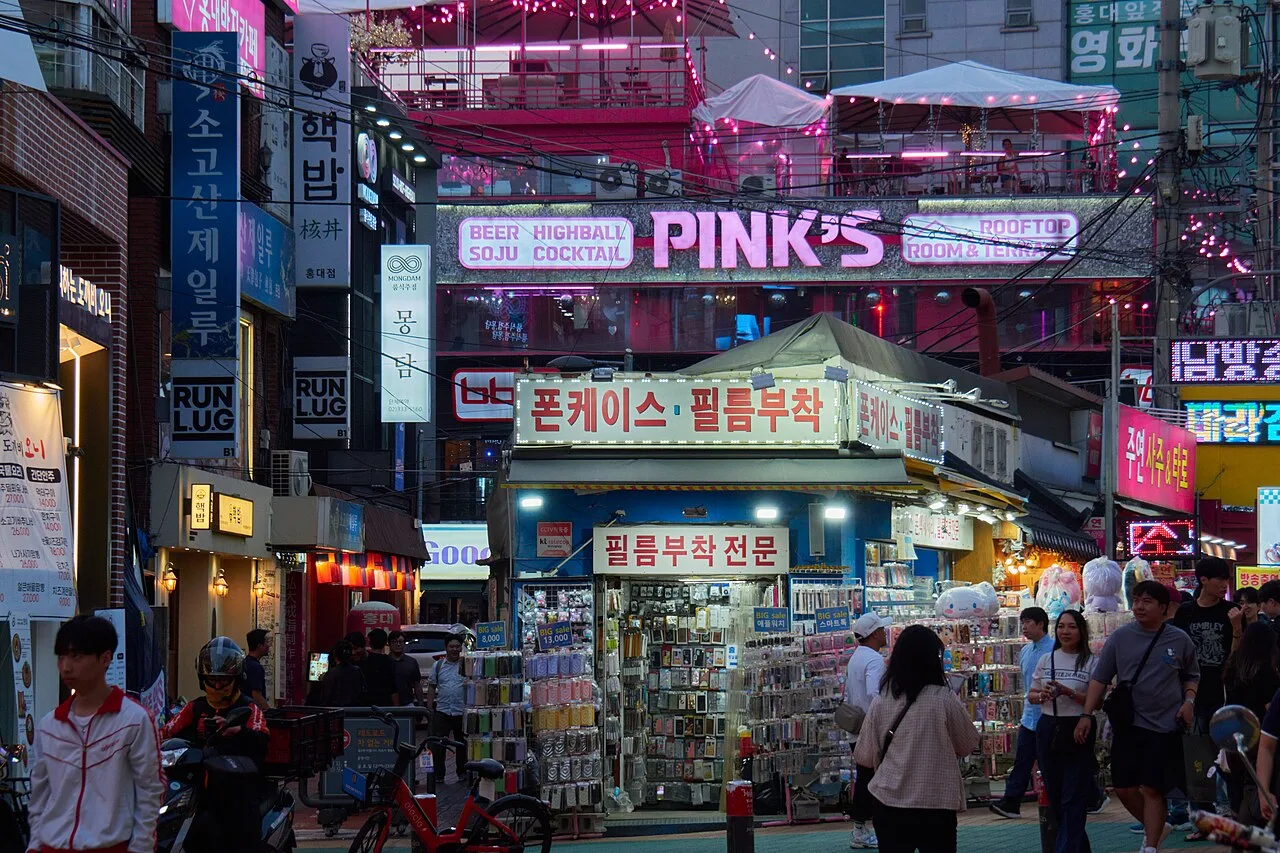 A Hongdae shopping street lined with small clothing and accessory shops under bright signs
