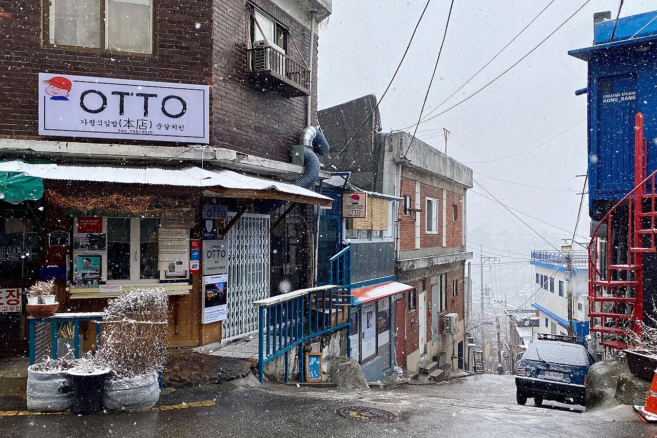 A steep Itaewon side street with small shops on a snowy day