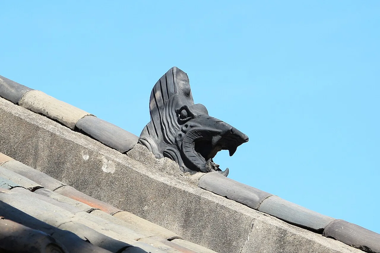 A carved stone guardian figure on the roof ridge of a Jongmyo building against a blue sky