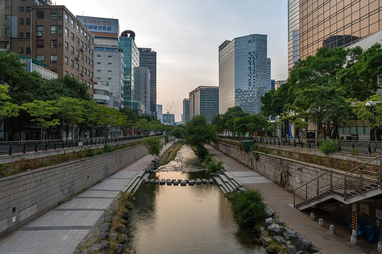 Cheonggyecheon Stream lined with trees and footpaths between office buildings at sunrise