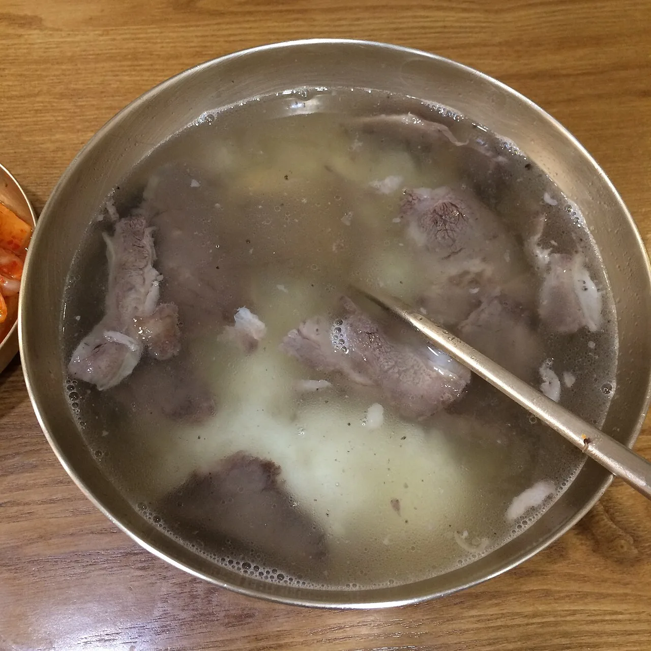 A brass bowl of clear gomtang beef soup with sliced beef and rice