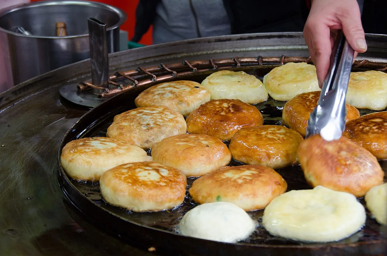 Hotteok sweet pancakes being pressed and fried on a griddle