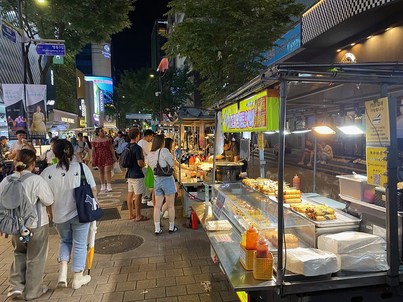 A Myeongdong street with food carts on one side and shoppers walking between shops