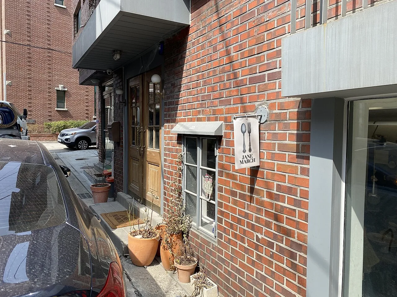 A red-brick building in Seongsu-dong with a small hanging shop sign, potted plants and a wooden door