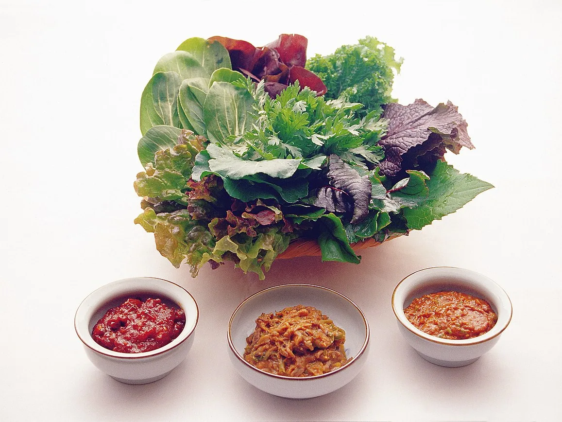 A basket of lettuce and leafy greens for ssam with three small bowls of dipping sauces