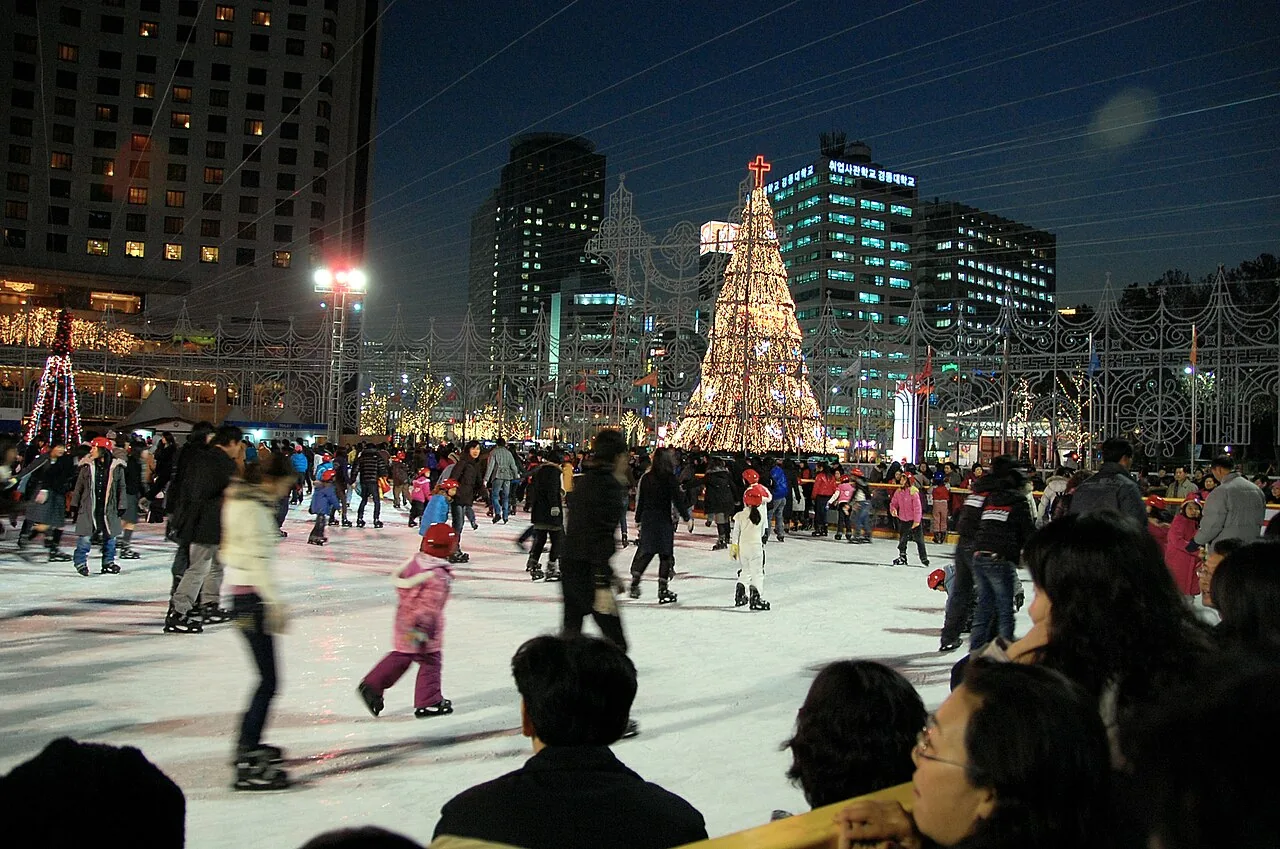 Skaters at the City Hall ice rink in Seoul with buildings behind