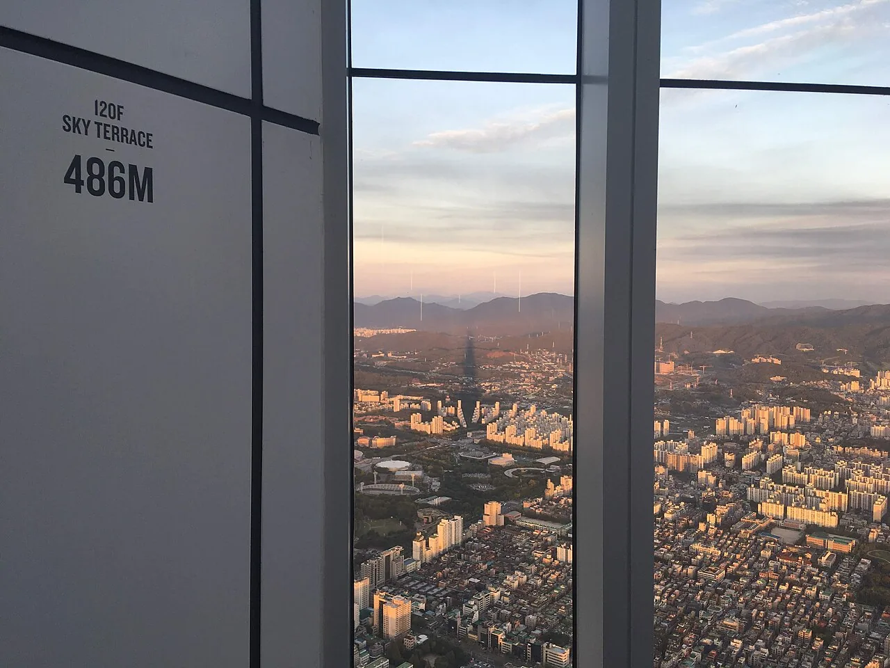 Floor sign reading 120F Sky Terrace 486M with a view over Seoul at sunset