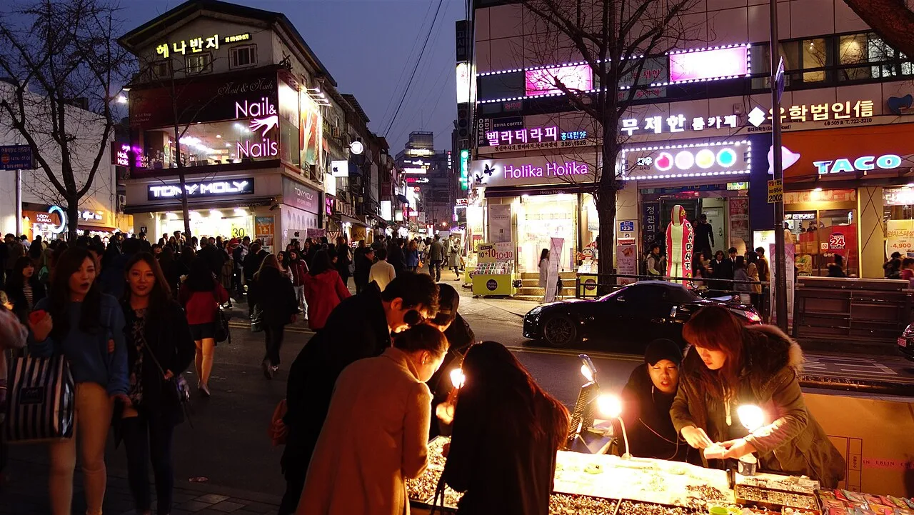 A busy Hongdae street at night lined with neon bar and club signs