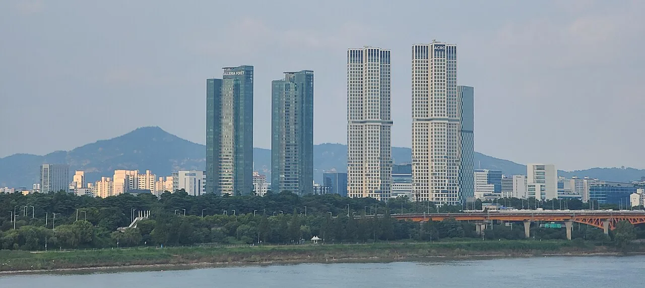 Seoul Forest's trees along the Han River with tall apartment towers behind, seen from Dongho Bridge