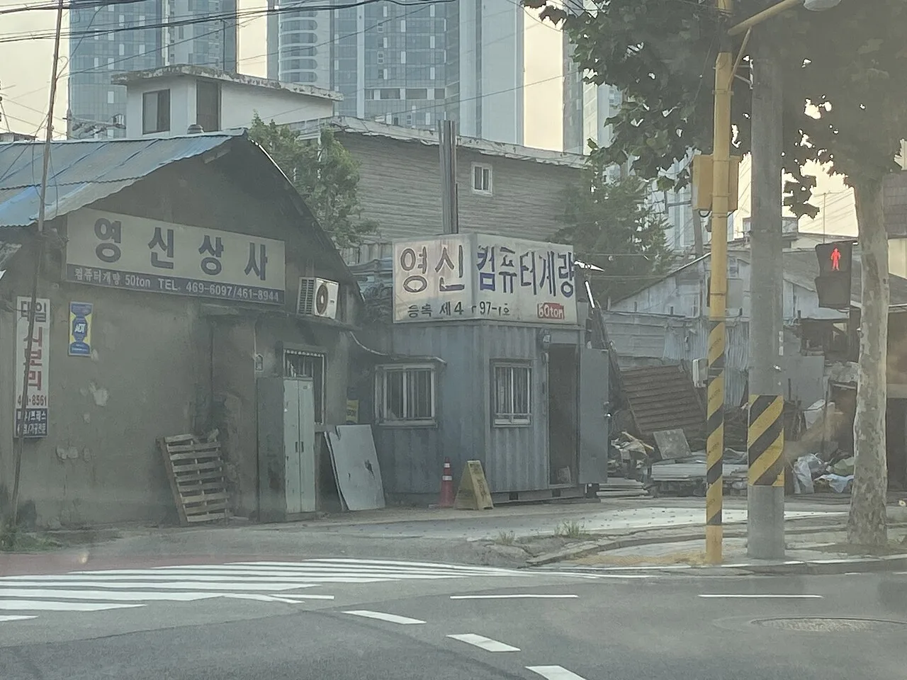 Old low-rise workshop buildings with Korean shop signs on a street corner in Seongsu-dong, with apartment towers behind
